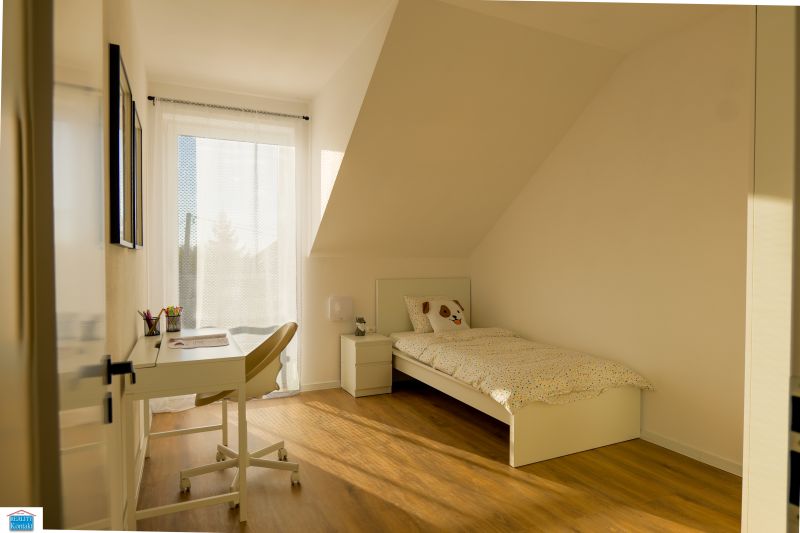 Bright children's room in a family house with a bed, desk, and wooden decor flooring.