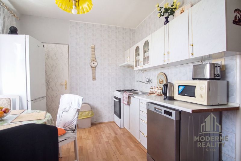 A kitchen in a 4-room apartment with a wooden decor floor and white cabinets.