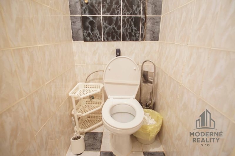 Bathroom in a 4-room apartment with a toilet, storage basket, and tiled wall.