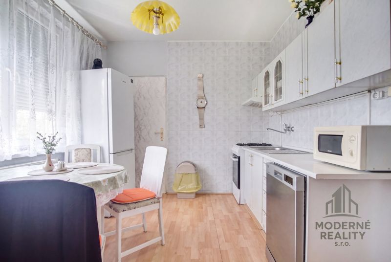 A kitchen in a 4-room apartment with white furniture, a table, and a wooden decor floor.