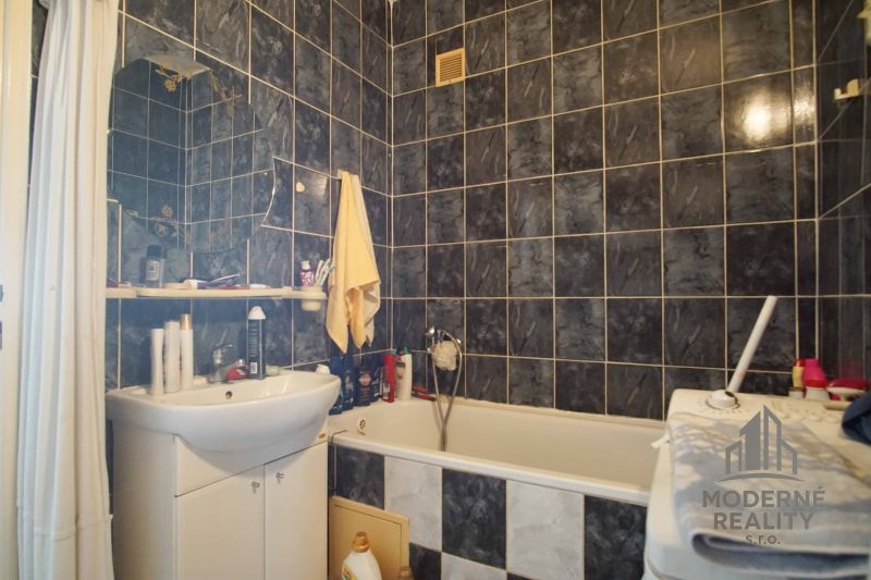 A bathroom with a shower curtain, bathtub, and black tiles in a 4-room apartment.