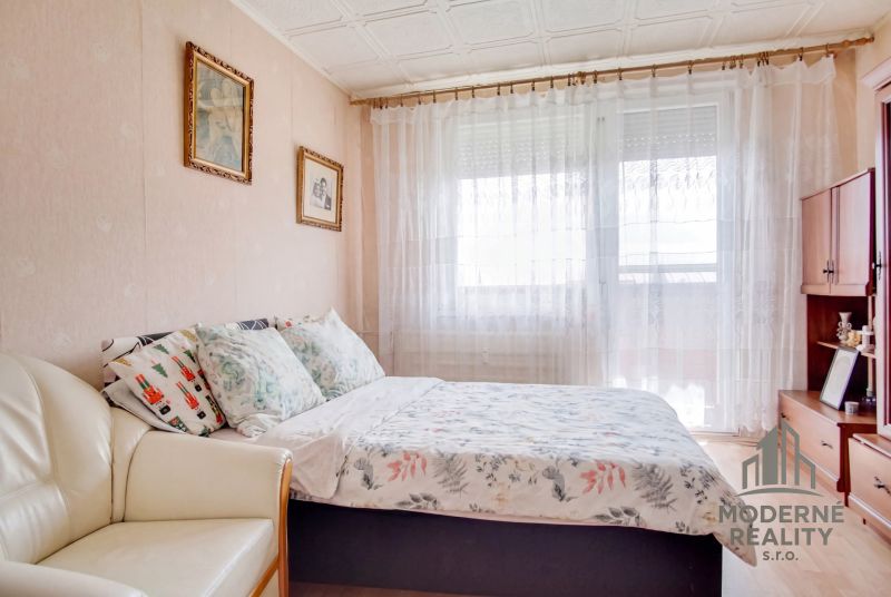 A bedroom in a 4-room apartment with decorative pillows and sheer curtains on the window.