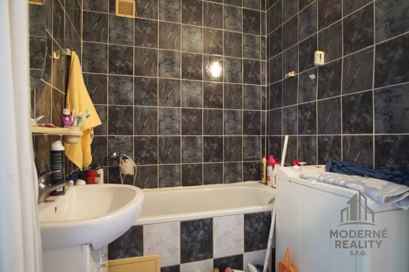 A bathroom in a 4-room apartment with dark tiles, a bathtub, and a washing machine.