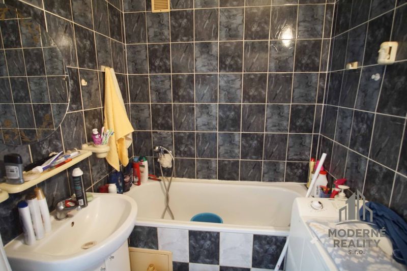 A bathroom in a 4-room apartment with a bathtub and darker tiles.