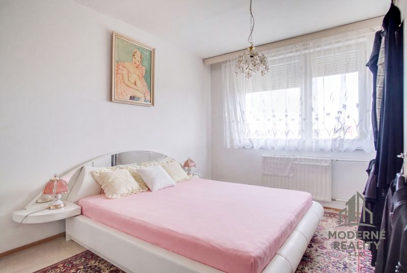A bedroom in a 4-room apartment with white walls, a decorative carpet, and a bed.