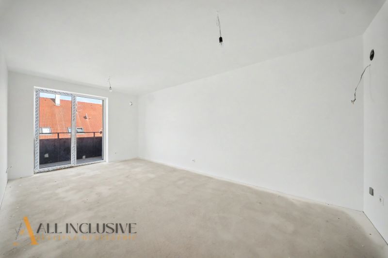A spacious room in a 2-room apartment with a large window and concrete floor.