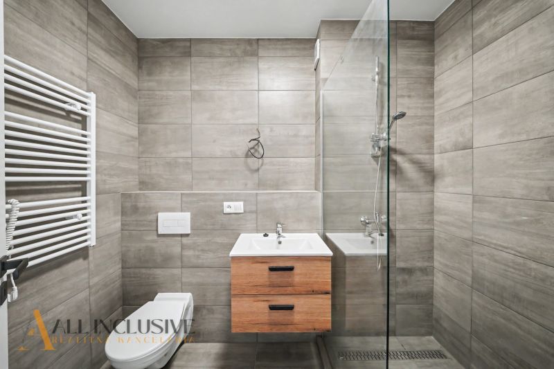 Bathroom in a 2-room apartment with a shower, sink, and wood-patterned tiles.