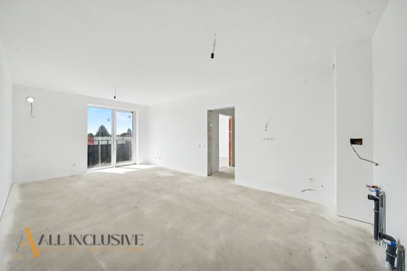 A spacious interior in an unfinished state with light walls and large windows in a 2-room apartment.