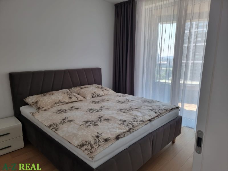 Bedroom in a 2-room apartment with a bed and a window with thin curtains.