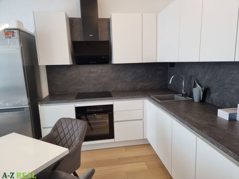 A kitchen in a 2-room apartment with white cabinets, a dark countertop, and a floor with a wood decor.