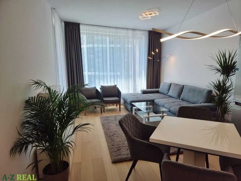 Living room in a 2-room apartment with a corner sofa, dining table, and wooden decor flooring.
