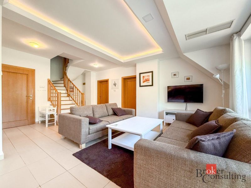 Living room with wood-patterned flooring, staircase, and sofa in a 5 or more room apartment.