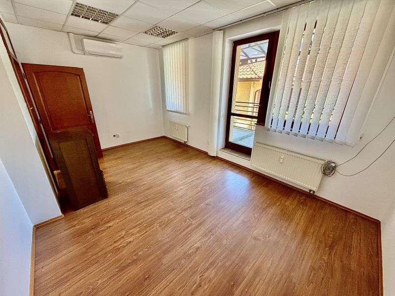 Interior of an office with wood-patterned flooring and vertical blinds.