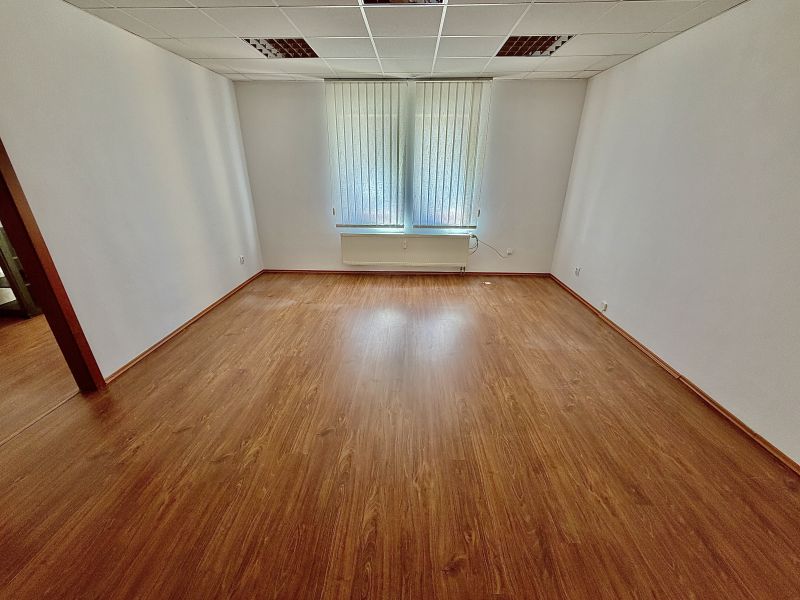 Living office with wood-patterned flooring and windows with vertical blinds.