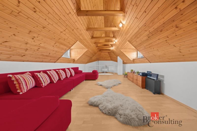 The attic of the cottage with a red sofa, wooden paneling, and a floor with a wooden decor.