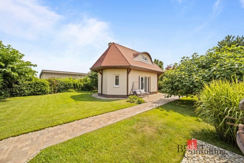 A cottage in Vojka nad Dunajom surrounded by a lawn and trees with a stone pathway.