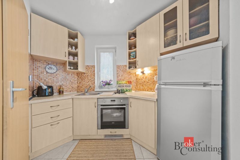 A kitchen in a cottage with light cabinets and an orange backsplash behind the sink.