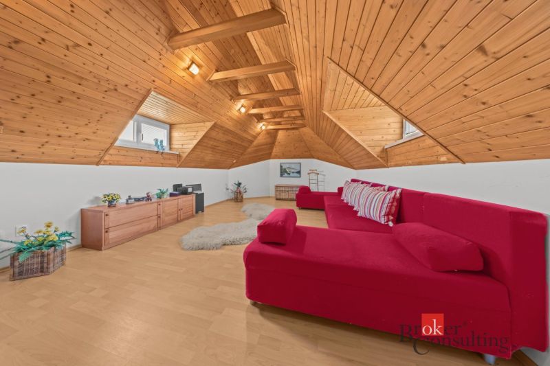 The attic of a cottage with a red sofa, wooden paneling, and a wooden-patterned floor.