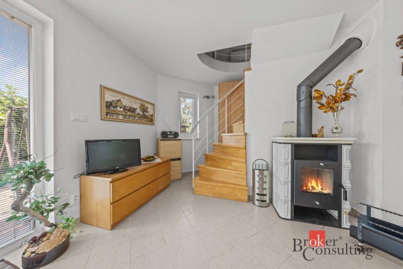 Interior of a cottage with a tiled stove, a television, and a wooden staircase.