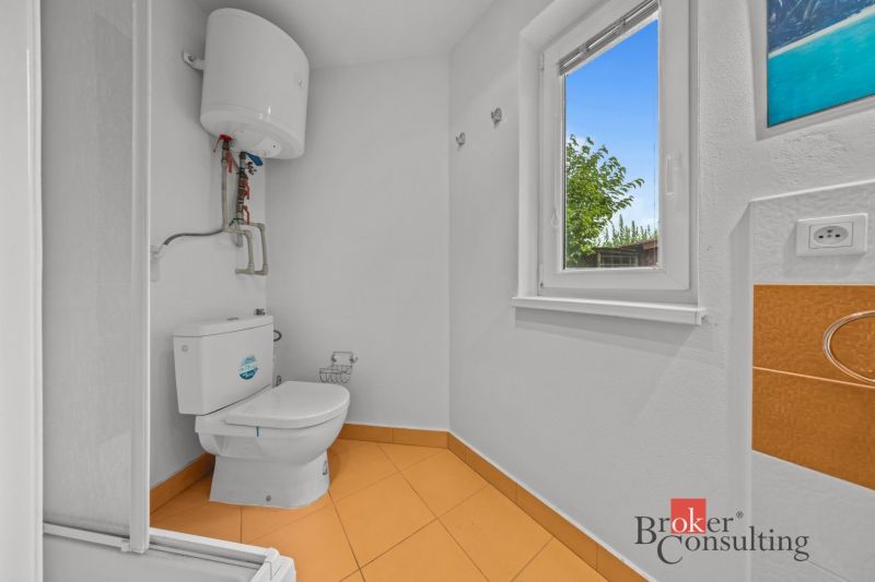 A bathroom with a window and a boiler, flooring with an orange design in a cottage.