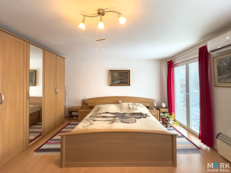 A bedroom in a family house with a wood-patterned floor, a large wardrobe, and balcony doors.