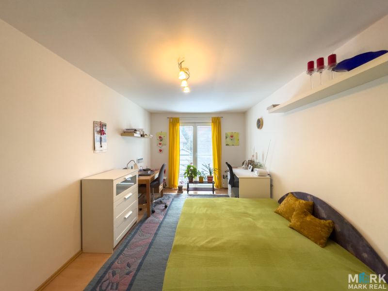 A room with a bed, a desk, a yellow curtain, and a floor with a wooden decor in a family house.