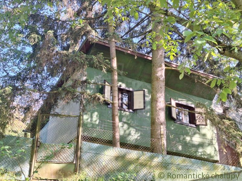 A cottage surrounded by trees in Kamenica nad Hronom, green facade, closed shutters.