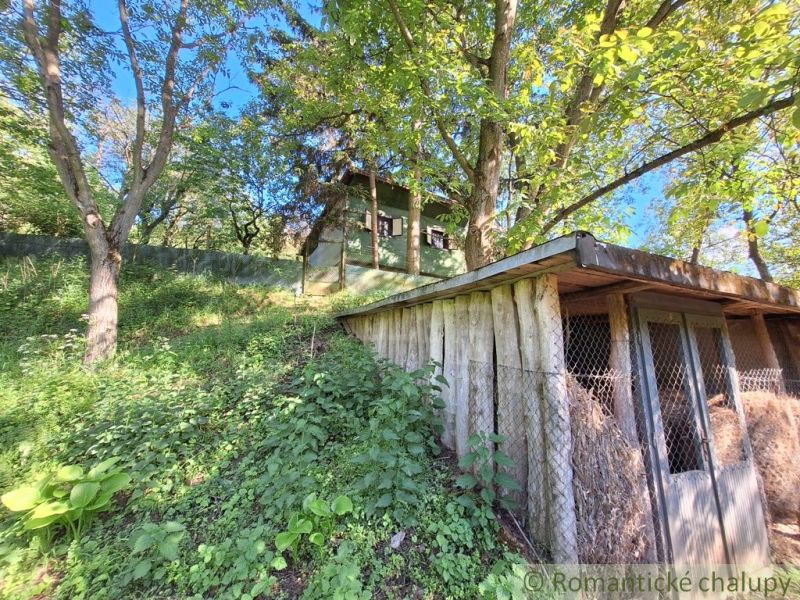 A cottage in Kamenica nad Hronom surrounded by greenery and trees, a wooden structure in the foreground.