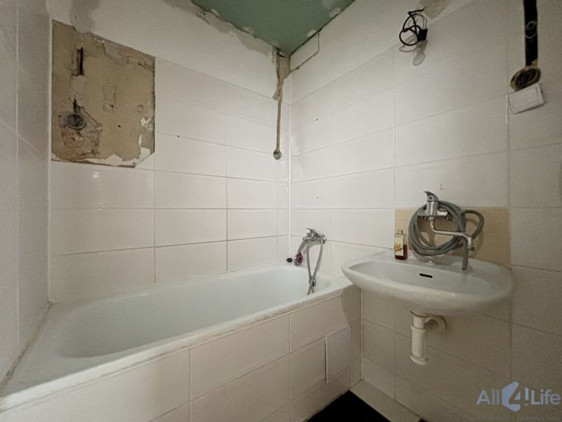 Bathroom in a 3-room apartment with a bathtub and a sink, white tiles on the walls.