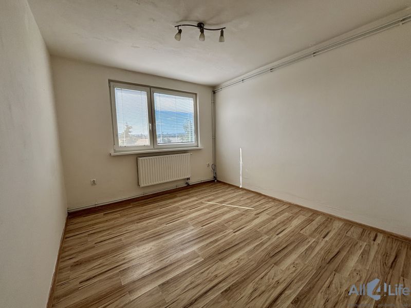A room in a 3-bedroom apartment with a large window and a wooden decor floor.