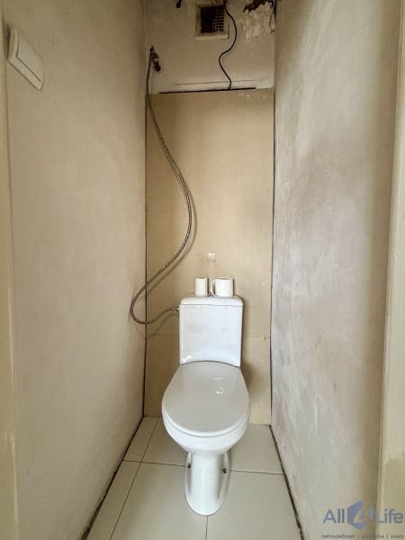 A bathroom in a 3-room apartment with bare walls and a screwed shower hose.