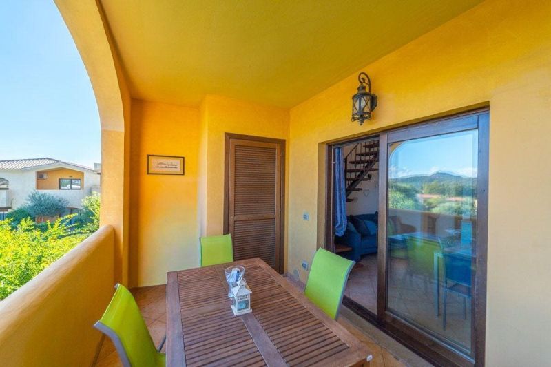 Terrace of a recreational apartment in Sardinia with a wooden table and colorful chairs.