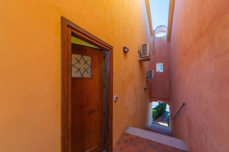 The hallway of a holiday apartment in Sardinia with colorful plastered walls and wooden doors.