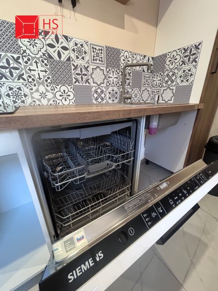 An open dishwasher in a 3-room apartment with mosaic tiles and wooden decor.