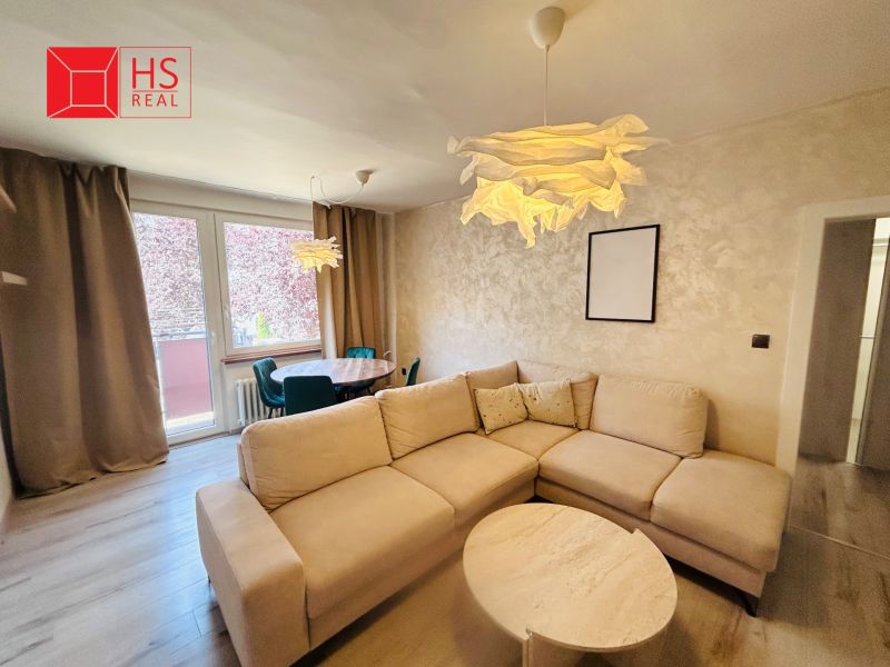 A room in a 3-room apartment with a sofa, a round table, and a floor with a wood decor.