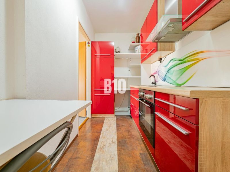 A kitchen in a 3-room apartment with vibrant red cabinets and a wood-patterned floor.