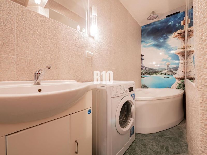 A bathroom of a three-room apartment with a shower, a washing machine, and colorful wall decoration.