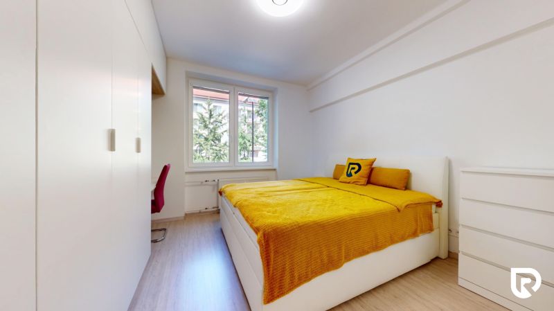 A bedroom with wood-patterned flooring, white furniture, and yellow bedding in a two-room apartment.