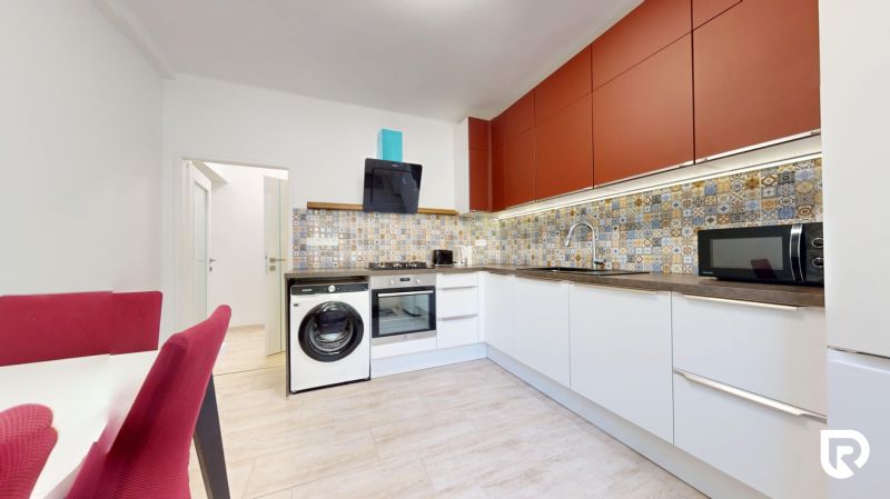 A kitchen in a 2-room apartment with colorful tiles, red cabinets, and a wooden-patterned floor.