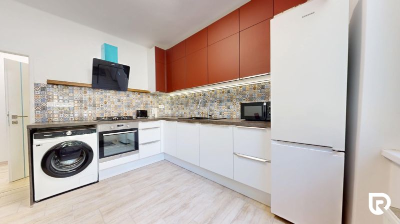 A kitchen in a 2-room apartment with equipment, patterned tiles, and a wooden decor floor.