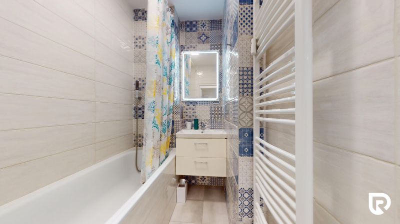 A bathroom with a bathtub, patterned tiles, and a mirror in a 2-room apartment.