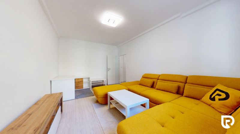 Living room of a two-room apartment with a yellow sofa and a white table.