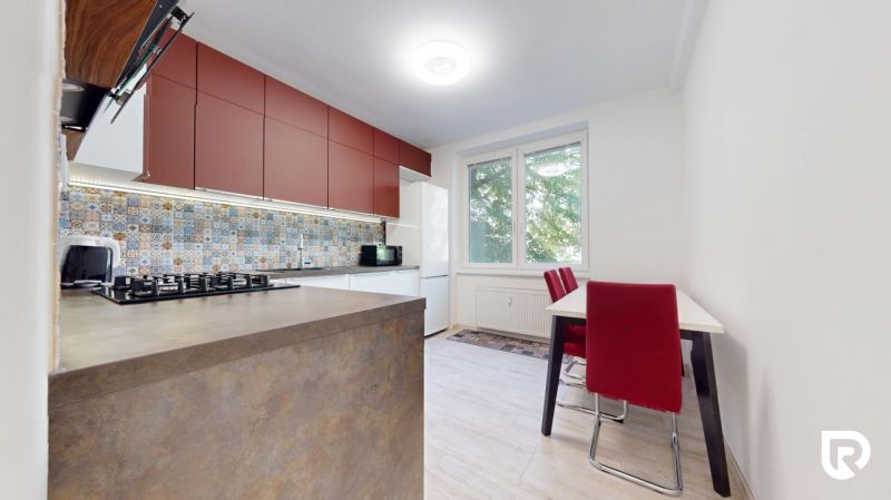 A kitchen in a 2-room apartment with colorful tiles, red cabinets, and a wood-patterned floor.