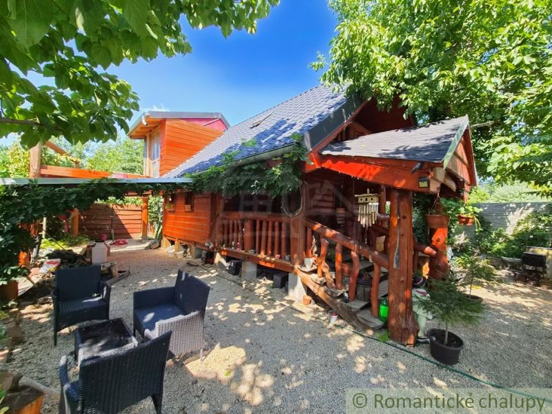 A log cabin in Lehoty with outdoor seating under trees in a pleasant natural environment.