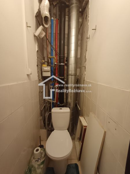 Bathroom in a 3-room apartment with a toilet and pipe installations on the wall.
