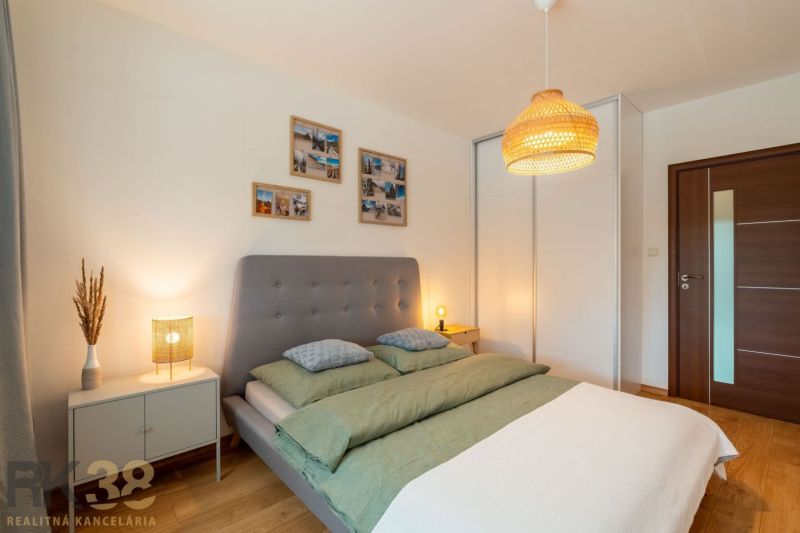 A bright bedroom with a bed, wood-patterned flooring, and a wardrobe in a two-room apartment.