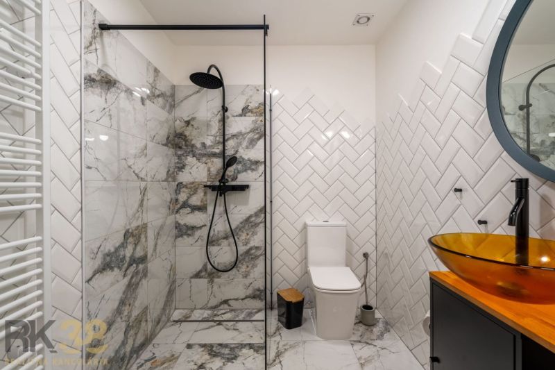 Bathroom with tiles and a glass shower enclosure in a 2-room apartment.