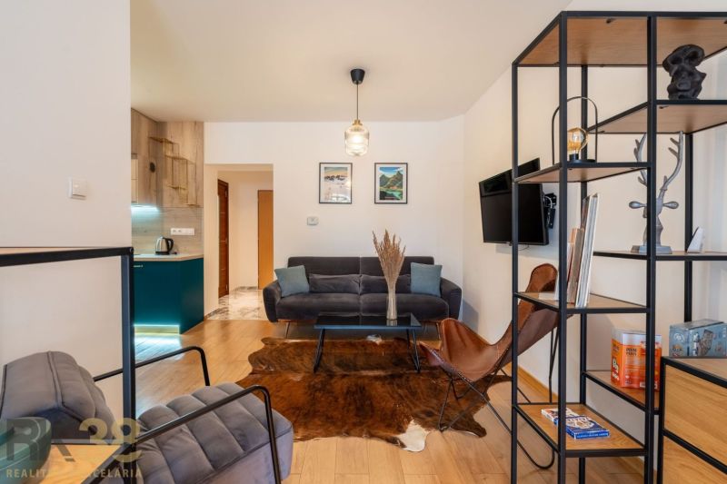 A room in a 2-room apartment with a sofa, armchairs, a shelf, and a floor with a wooden decor.