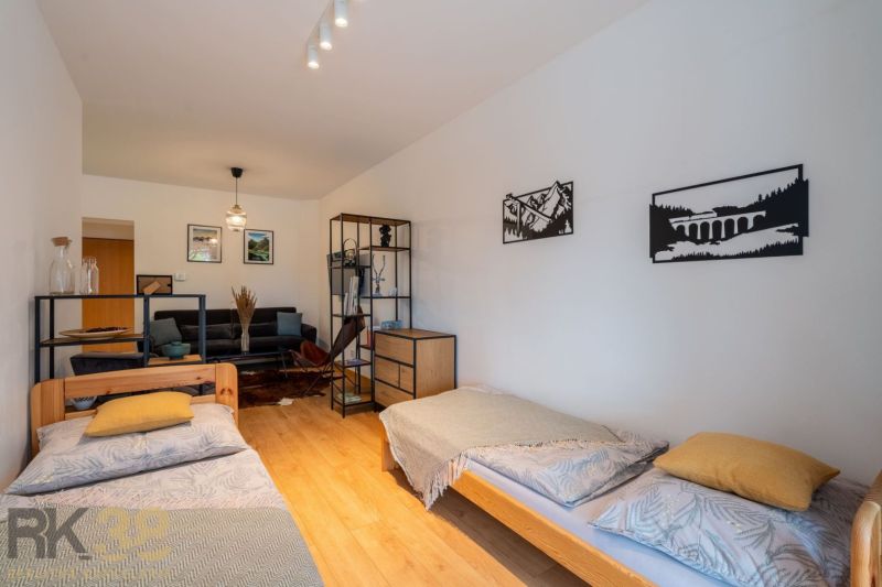 Interior of a 2-room apartment with a wooden decor floor, beds, sofa, and decorations.