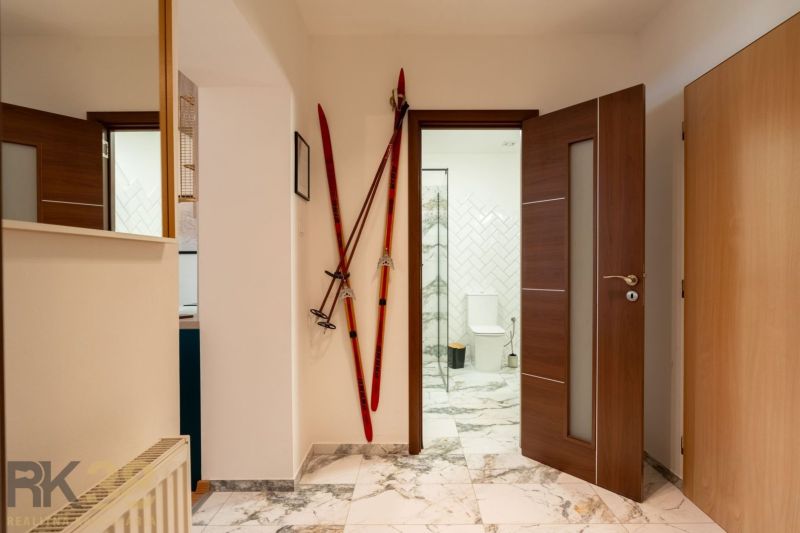 Interior of a 2-room apartment with ski poles by the door and a bathroom in the background.